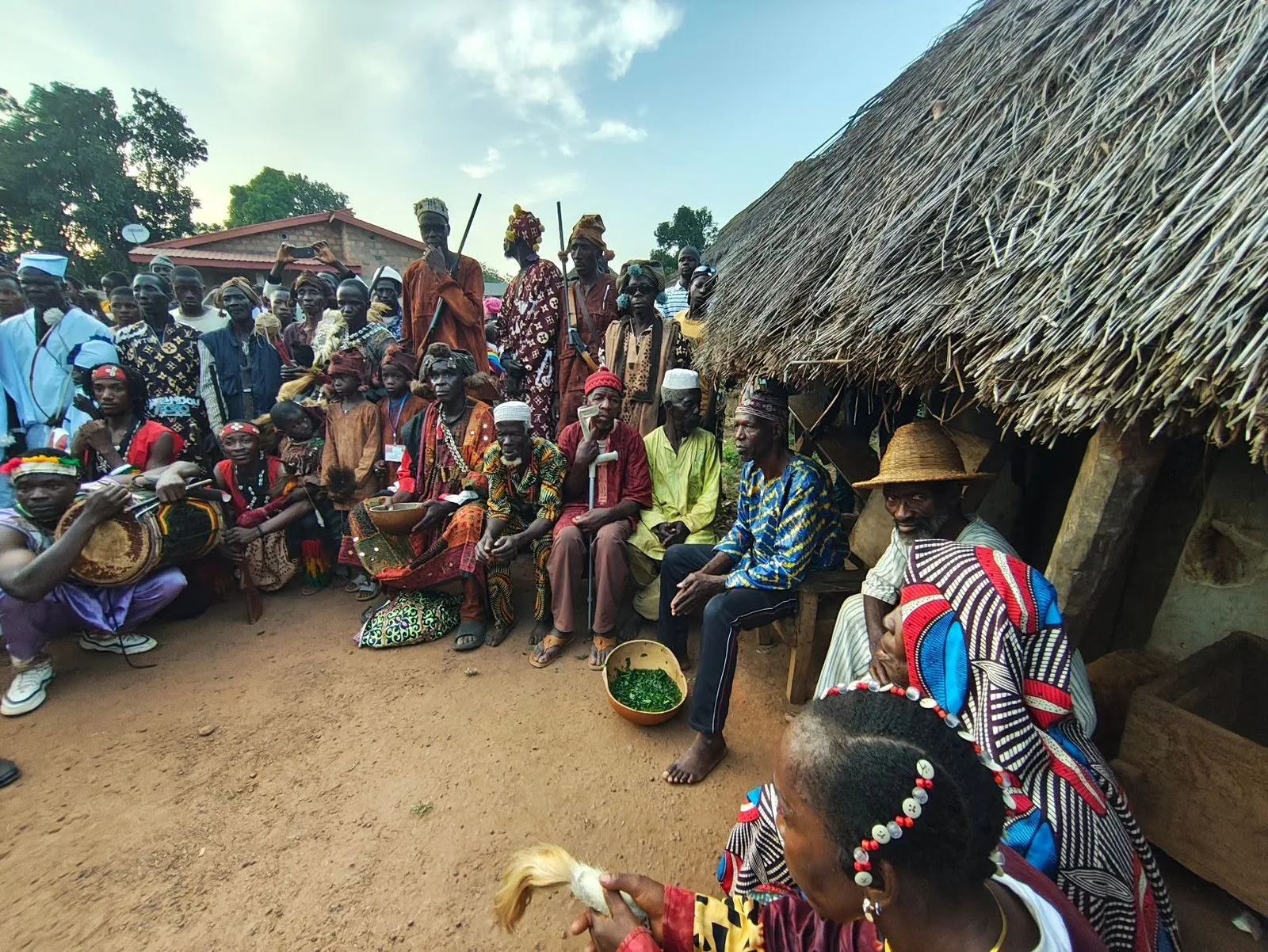 Village elders and musicians gathered beside a thatched hut