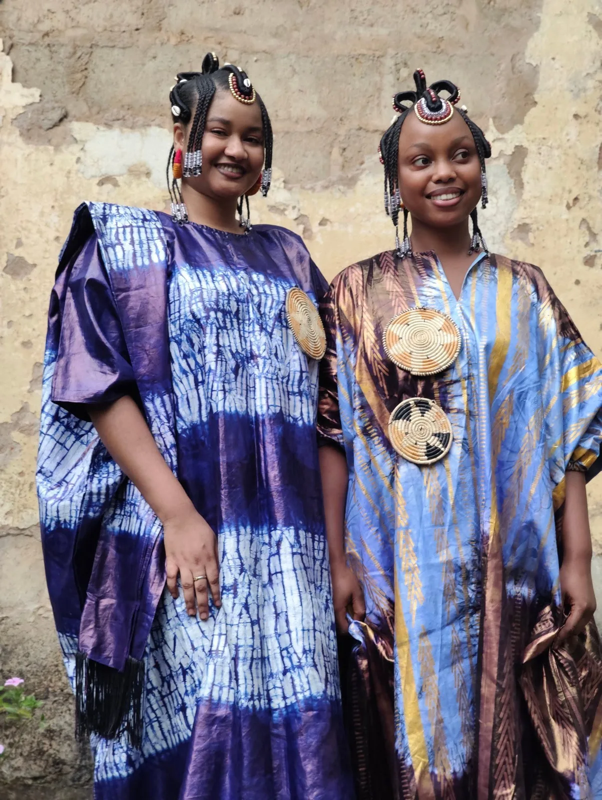 Two women in indigo tie-dye dresses with traditional hair ornaments