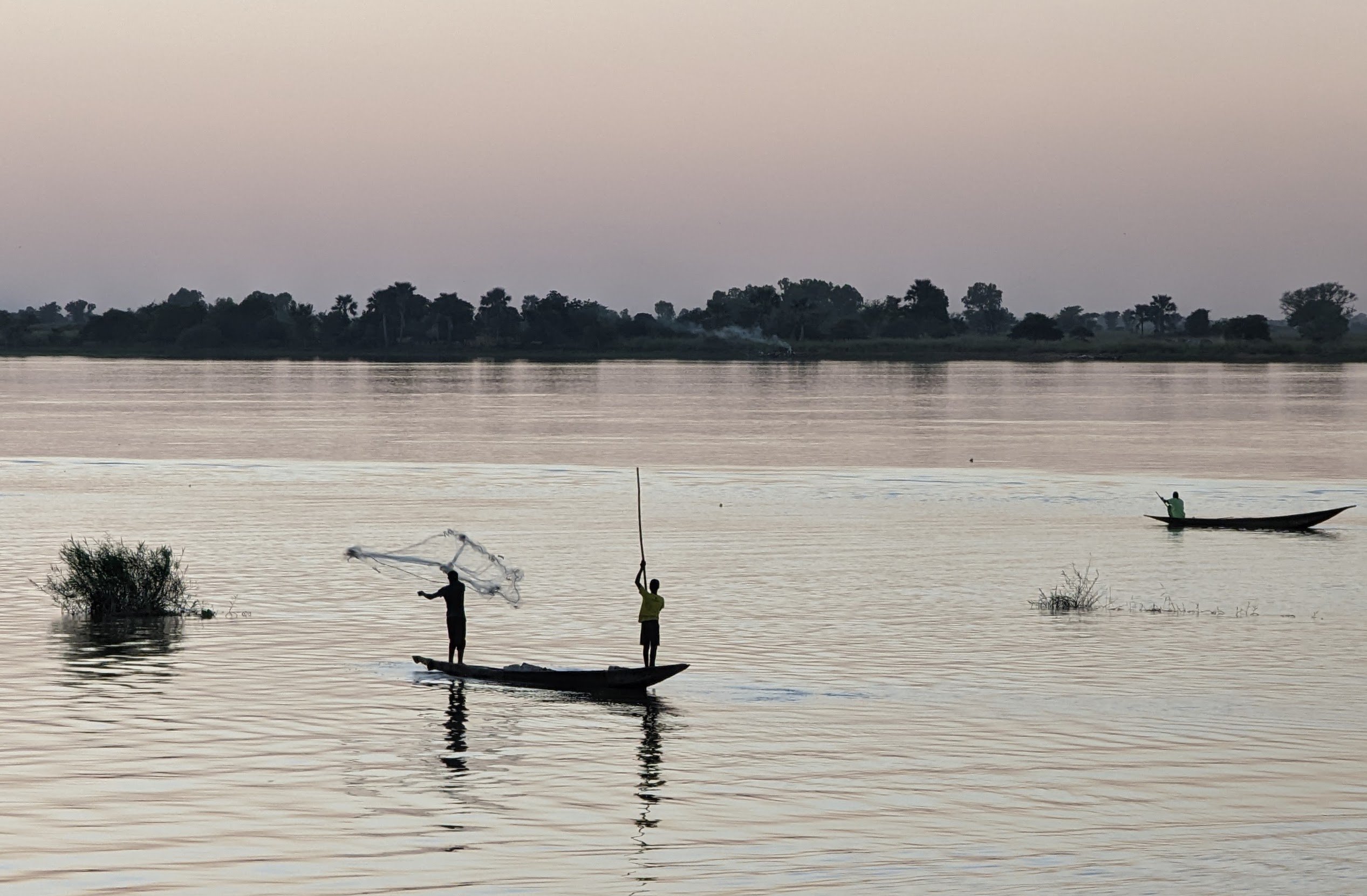 Fishermen casting nets from a pirogue on the Niger River at dusk